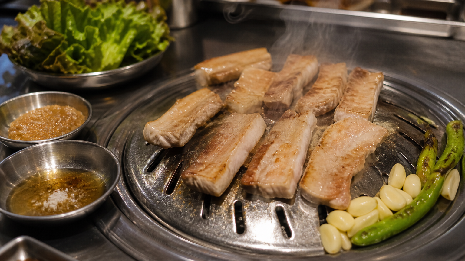 Samgyeopsal on the grill. The meat is completely unseasoned, and everything sharp is in a dish on the side
